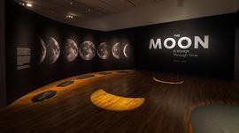 An exhibition space with "The Moon" written on a black wall and images of the moon on the wall.